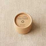Round brown container with 'Small Colorful Stitch Markers' text on a beige fabric background
