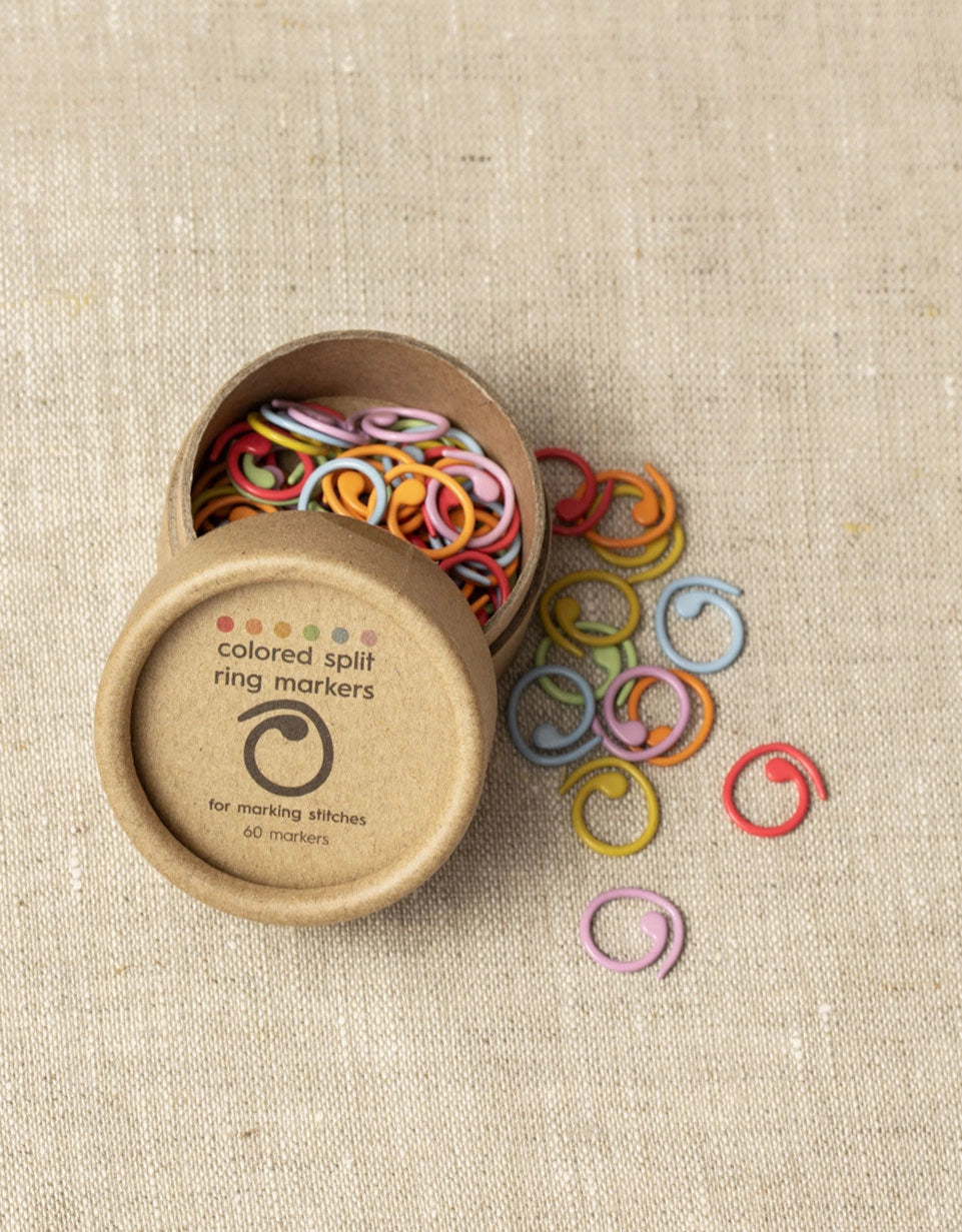 Colorful split ring markers spilling out of a cardboard container on a beige fabric background