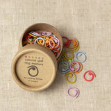 Colorful split ring markers spilling out of a cardboard container on a beige fabric background