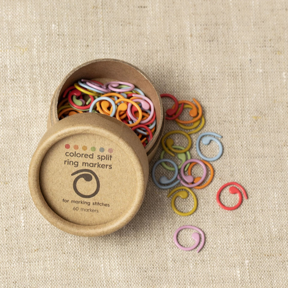 Colorful split ring markers spilling out of a cardboard container on a beige fabric background
