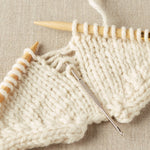 Knitted fabric with wooden knitting needles and a metal crochet hook fixing dropped stitches on a beige background