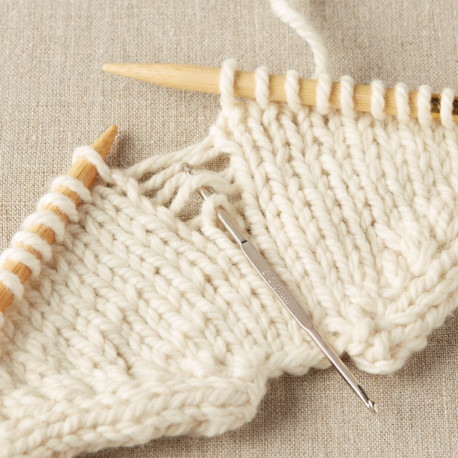 Knitted fabric with wooden knitting needles and a metal crochet hook fixing dropped stitches on a beige background