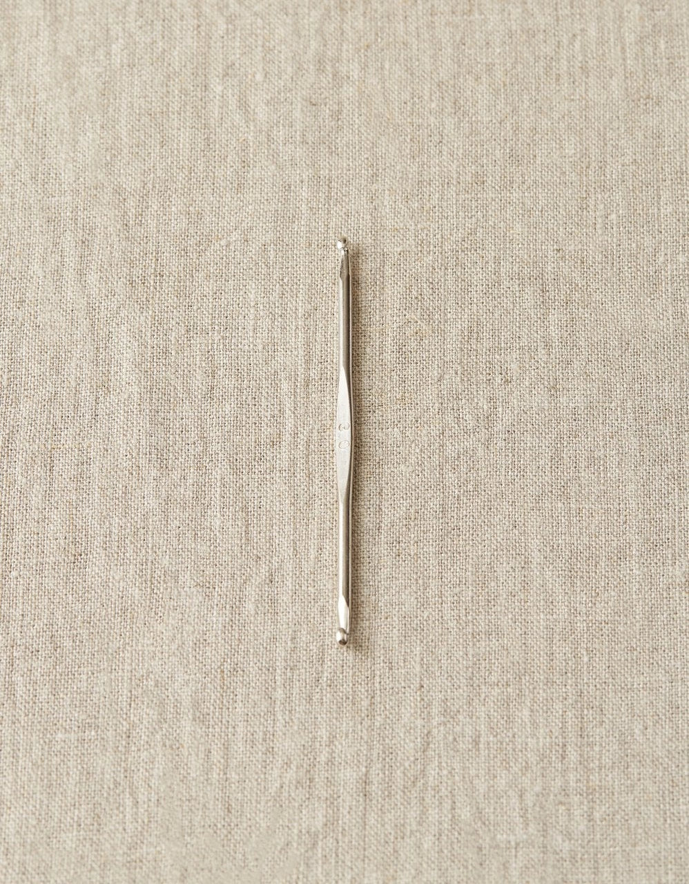 Silver crochet hook on a beige fabric background