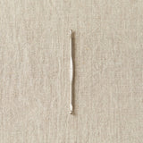 Silver crochet hook on a beige fabric background