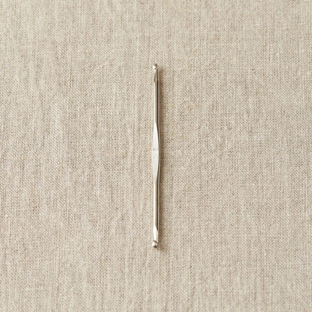 Silver crochet hook on a beige fabric background