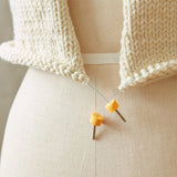 Knitted garment on a mannequin with orange stitch stoppers on circular needles.