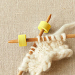 Knitting needles with yellow foam stitch stoppers on a beige fabric background