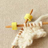 Knitting needles with yellow foam stitch stoppers on a beige fabric background