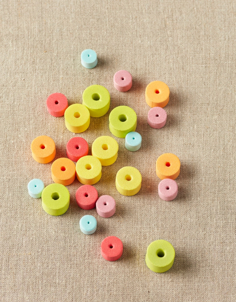 Rainbow colored stitch stoppers on a textured beige surface