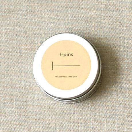 Tin container with 't-pins' label on a textured beige background