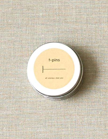 Tin container with 't-pins' label on a textured beige background