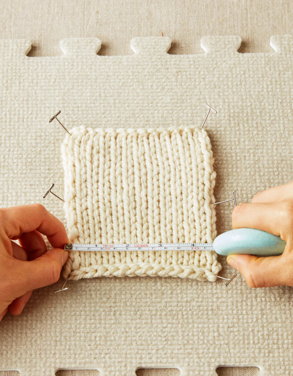 Person measuring a knitted sample with a ruler on a textured surface