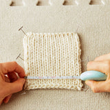 Person measuring a knitted sample with a ruler on a textured surface