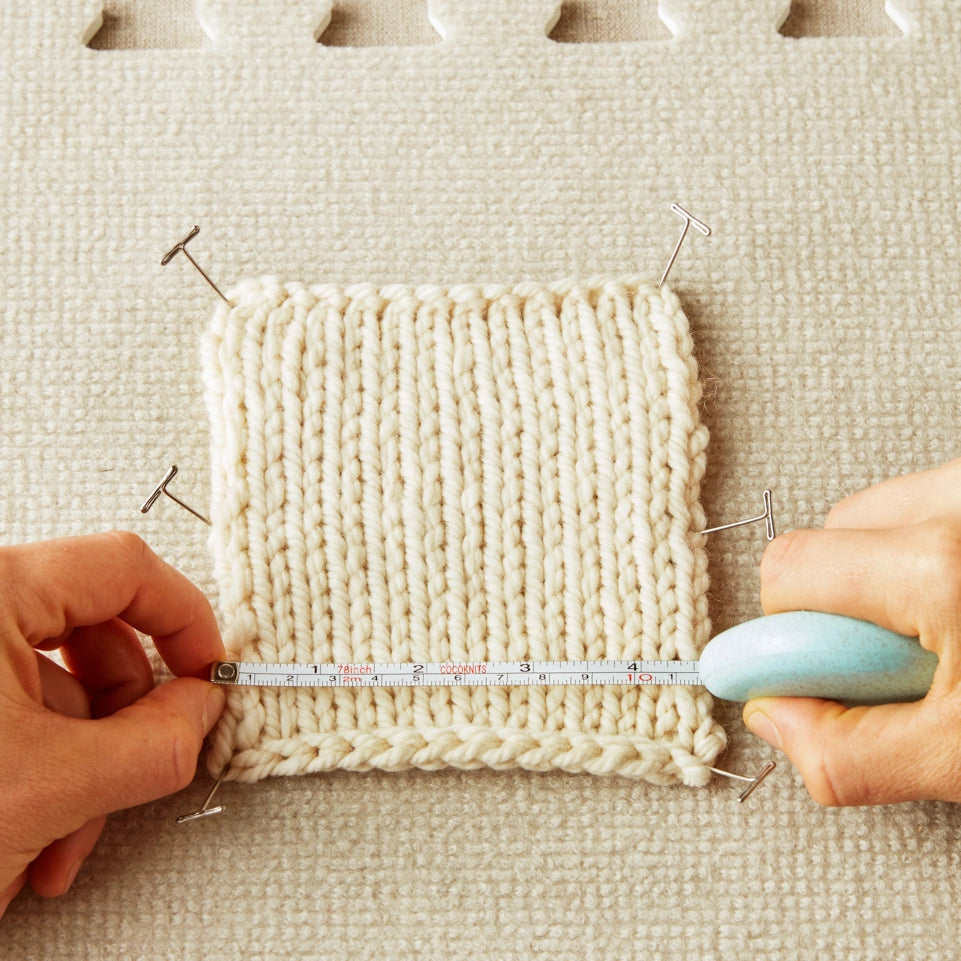Person measuring a knitted sample with a tape measure on a textured surface