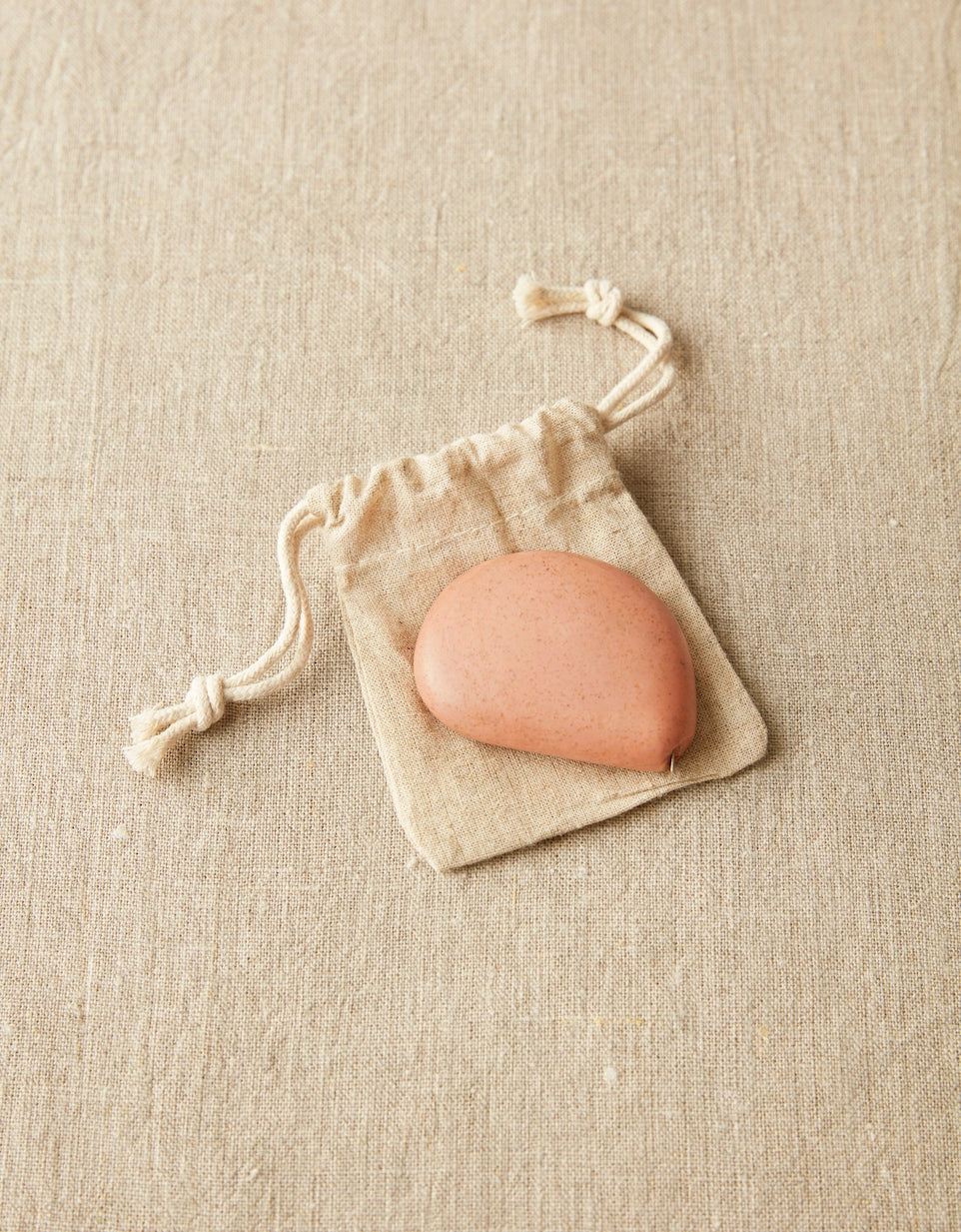 Clay colored tape measure on drawstring bag on a beige fabric background