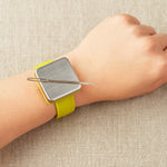 Magnetic slap bracelet with a yellow strap on a wrist with a tapestry needle attatched to the magnet against a beige background
