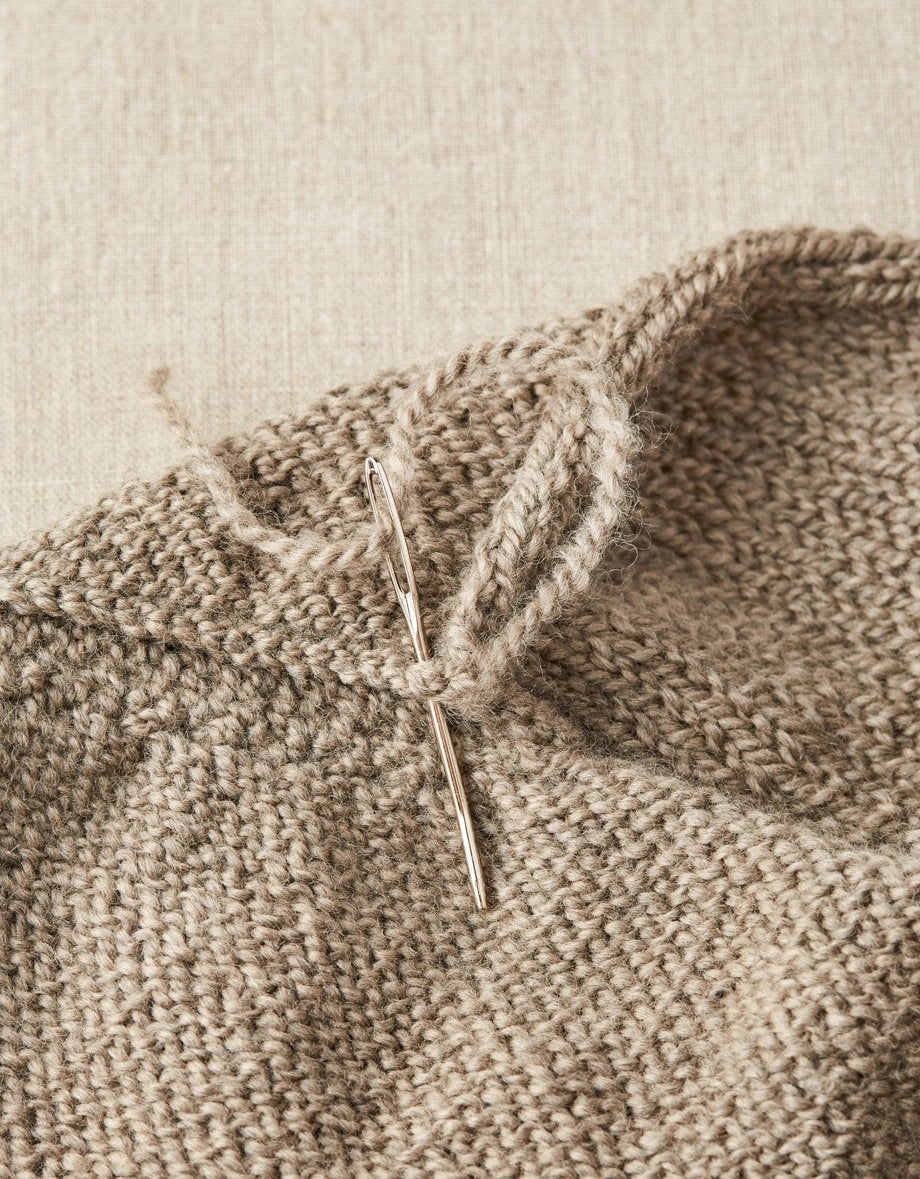 Close-up of a knitted fabric with a needle inserted into the work on a beige background
