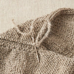 Close-up of a knitted fabric with a needle inserted into the work on a beige background
