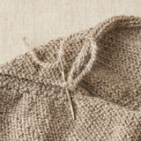 Close-up of a knitted fabric with a needle inserted into the work on a beige background