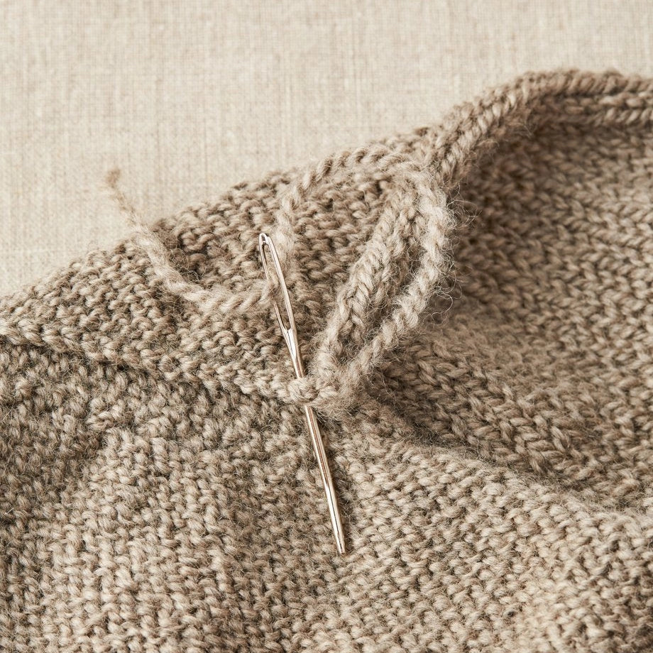 Close-up of a knitted fabric with a needle inserted into the work on a beige background