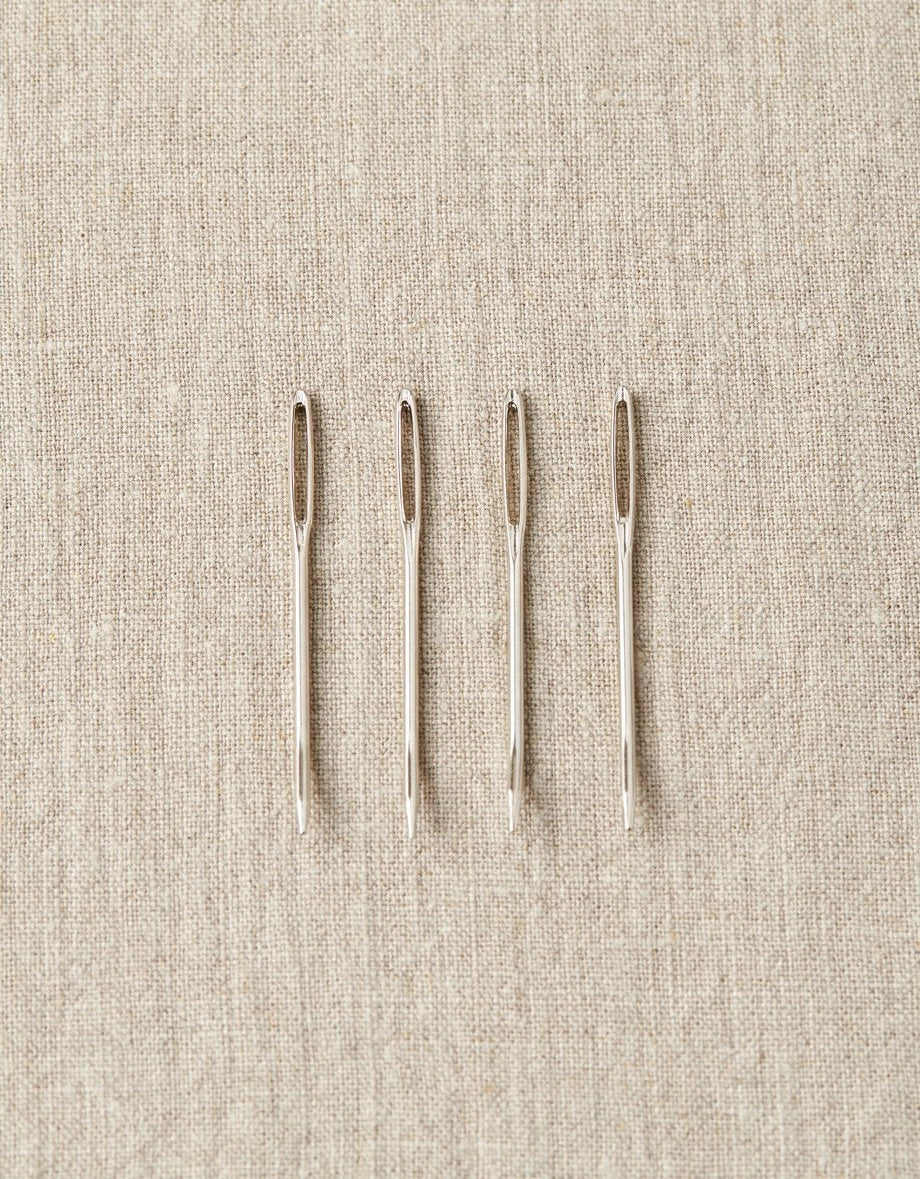 Four tapestry needles on a beige fabric background
