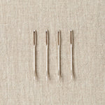 Four tapestry needles on a beige fabric background