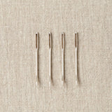 Four tapestry needles on a beige fabric background