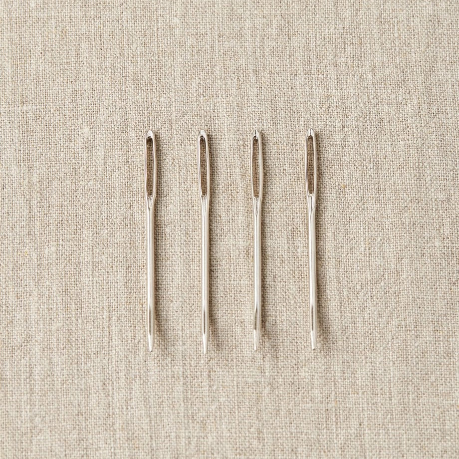 Four tapestry needles on a beige fabric background