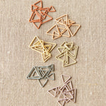 Set of colored triangle stitch markers on a textured beige background
