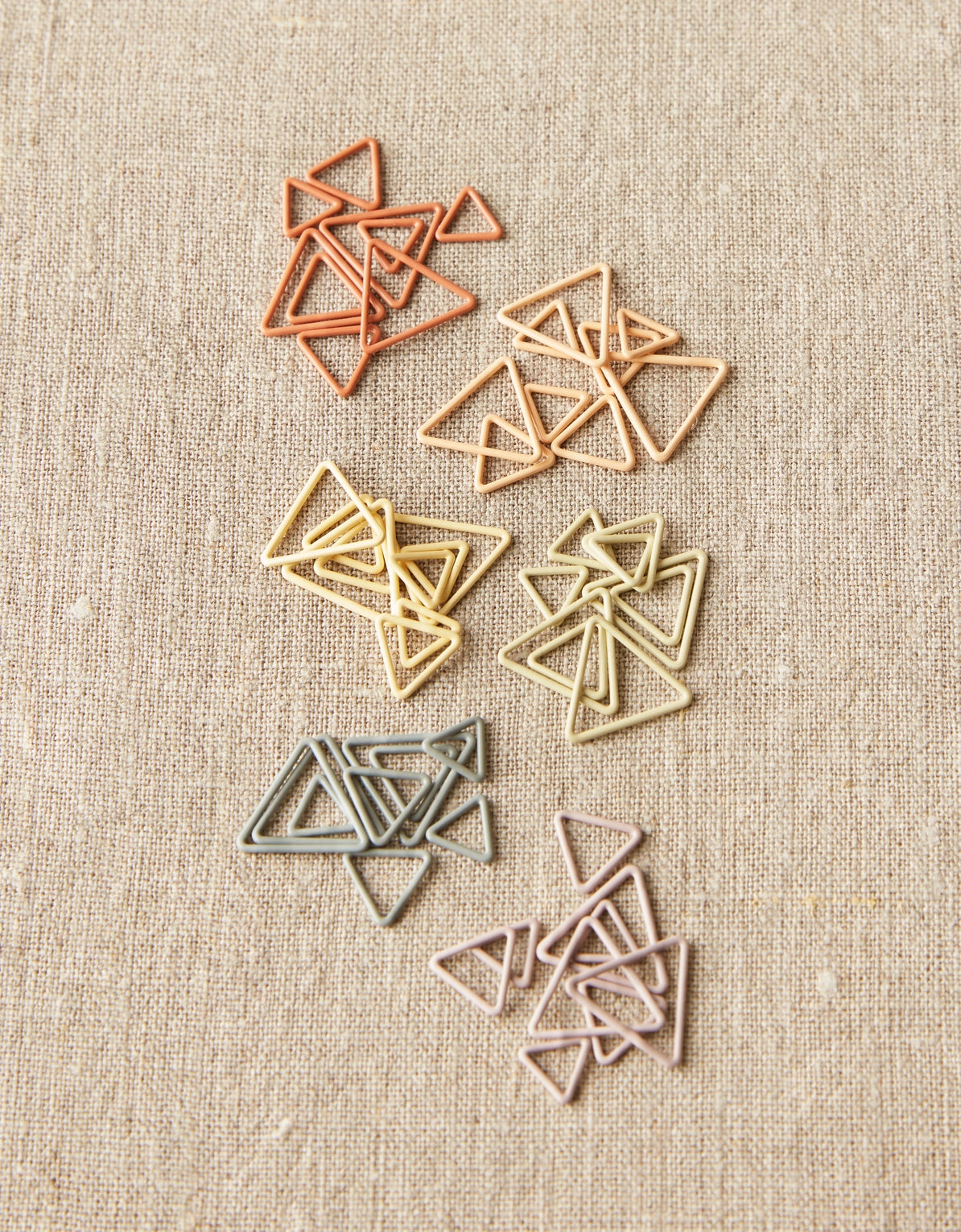 Set of colored triangle stitch markers on a textured beige background