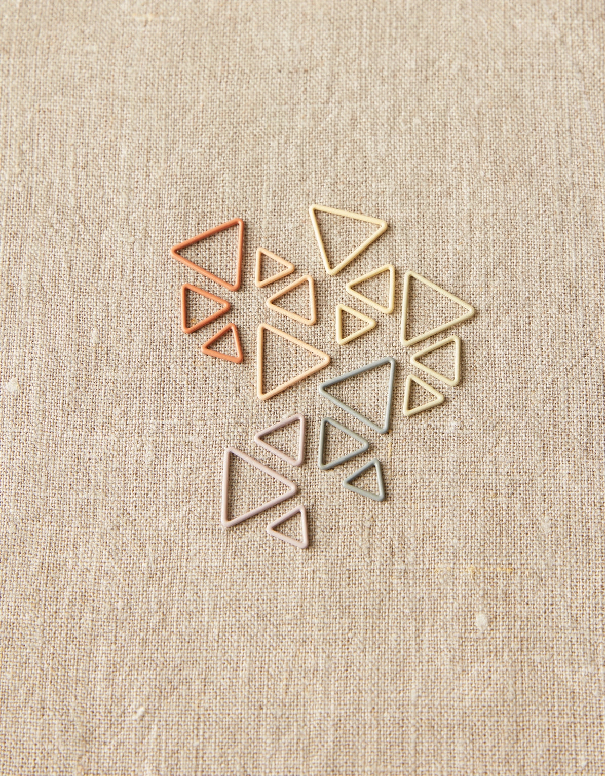 Set of geometric triangle-shaped stitch markers on a beige fabric background