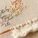 Wooden knitting needle with yarn and triangle shaped stitch markers on the needle on a textured fabric background