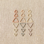 Set of different sizes of triangle-shaped stitch markers on a beige fabric background