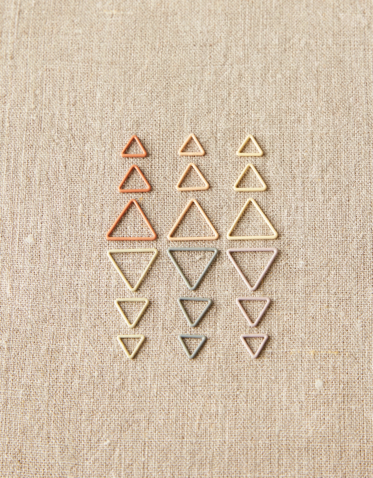 Set of different sizes of triangle-shaped stitch markers on a beige fabric background