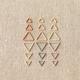 Set of different sizes of triangle-shaped stitch markers on a beige fabric background