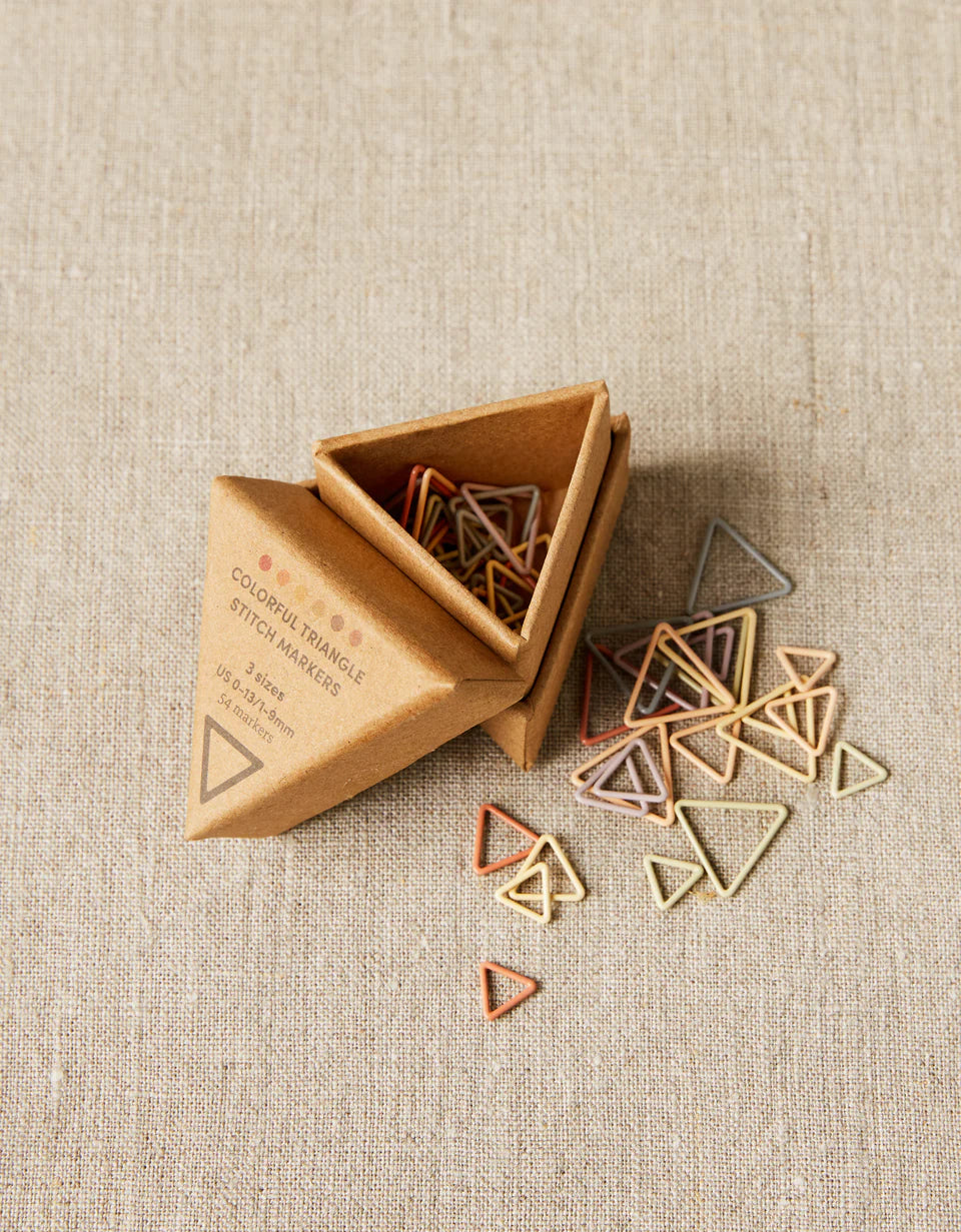 Triangle-shaped stitch markers in a cardboard box on a beige fabric background