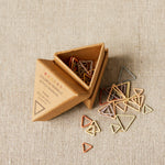 Triangle-shaped stitch markers in a cardboard box on a beige fabric background