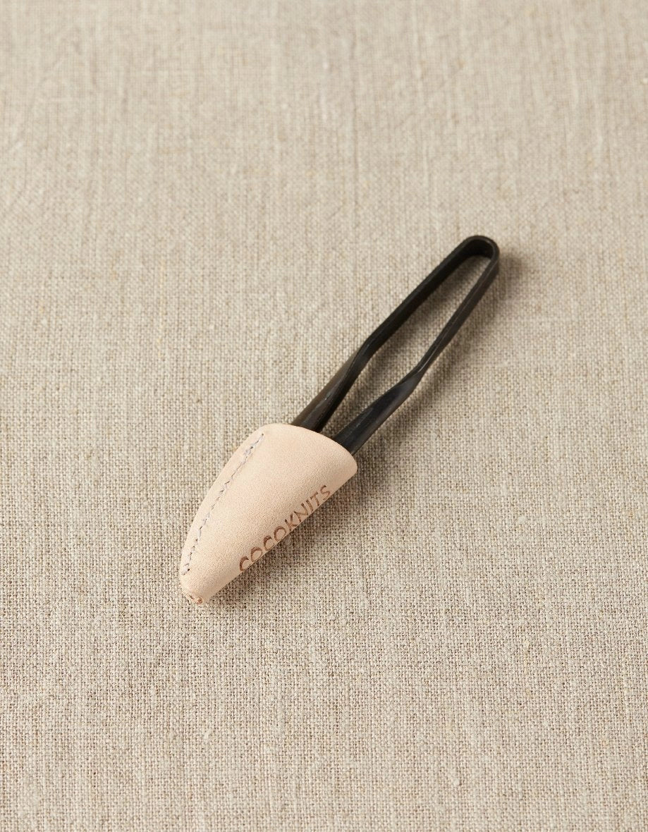 Black thread snips inside a leather case on a beige fabric background
