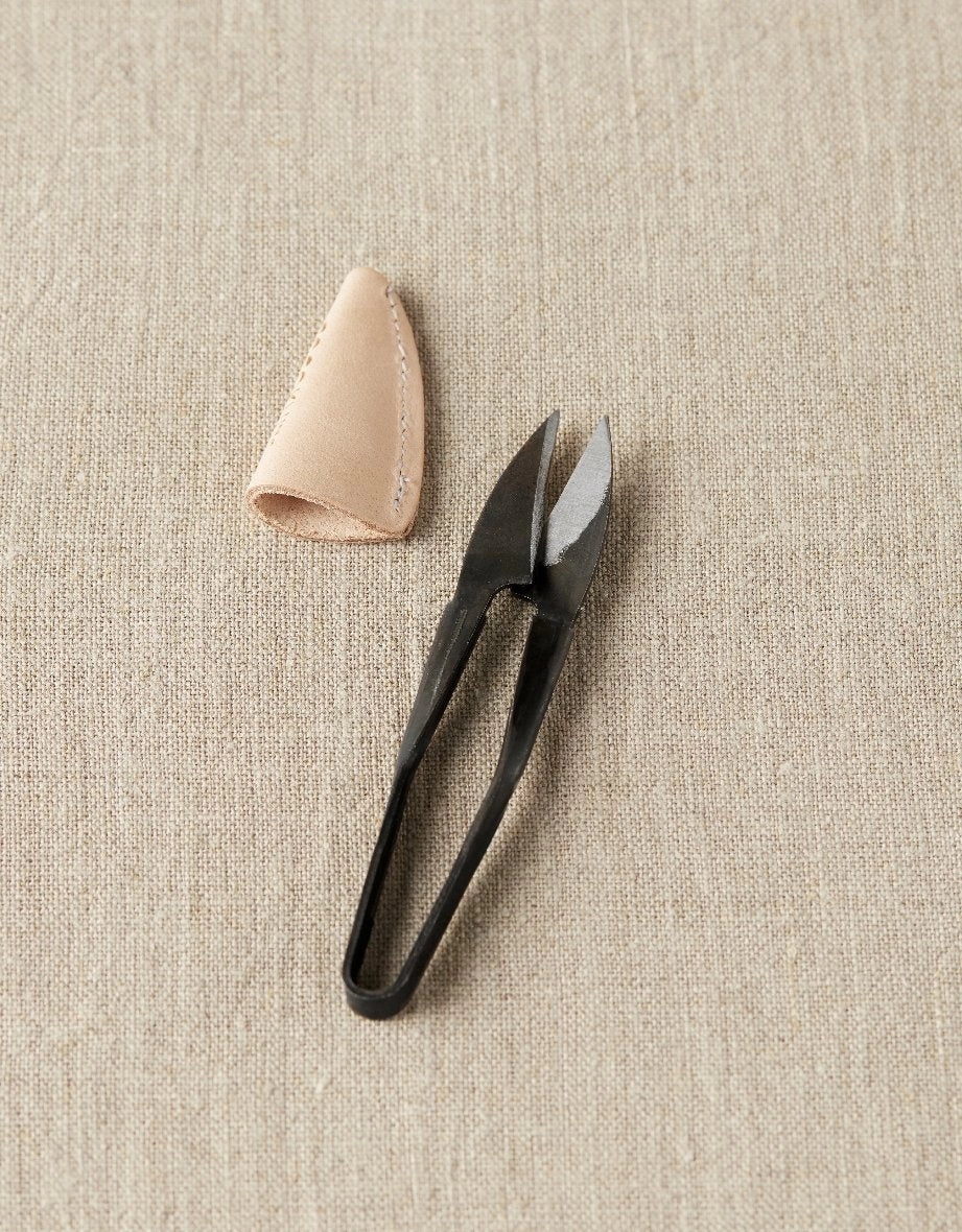Black yarn snips and beige leather case on a beige fabric background