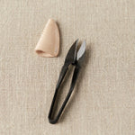 Black yarn snips and beige leather case on a beige fabric background
