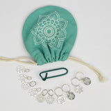A set of stainless steel knitting needles, a knitting bag with a floral pattern, and a needle threader, all arranged on a white surface.