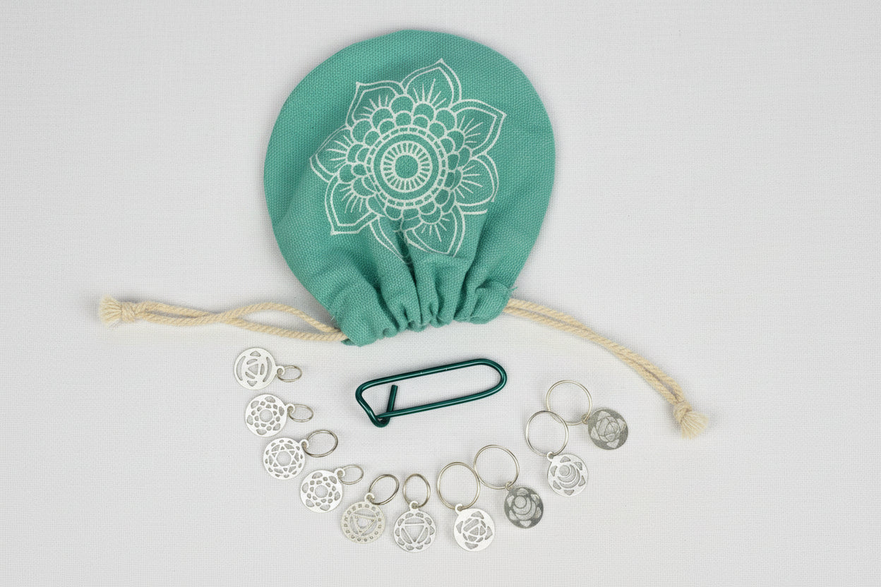 A set of stainless steel knitting needles, a knitting bag with a floral pattern, and a needle threader, all arranged on a white surface.