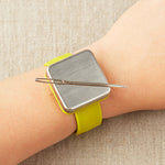Yellow magnetic slap bracelet on a person's wrist with a darning needle attatched to the magnet.