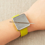 Yellow magnetic slap bracelet on a person's wrist with a darning needle attatched to the magnet.