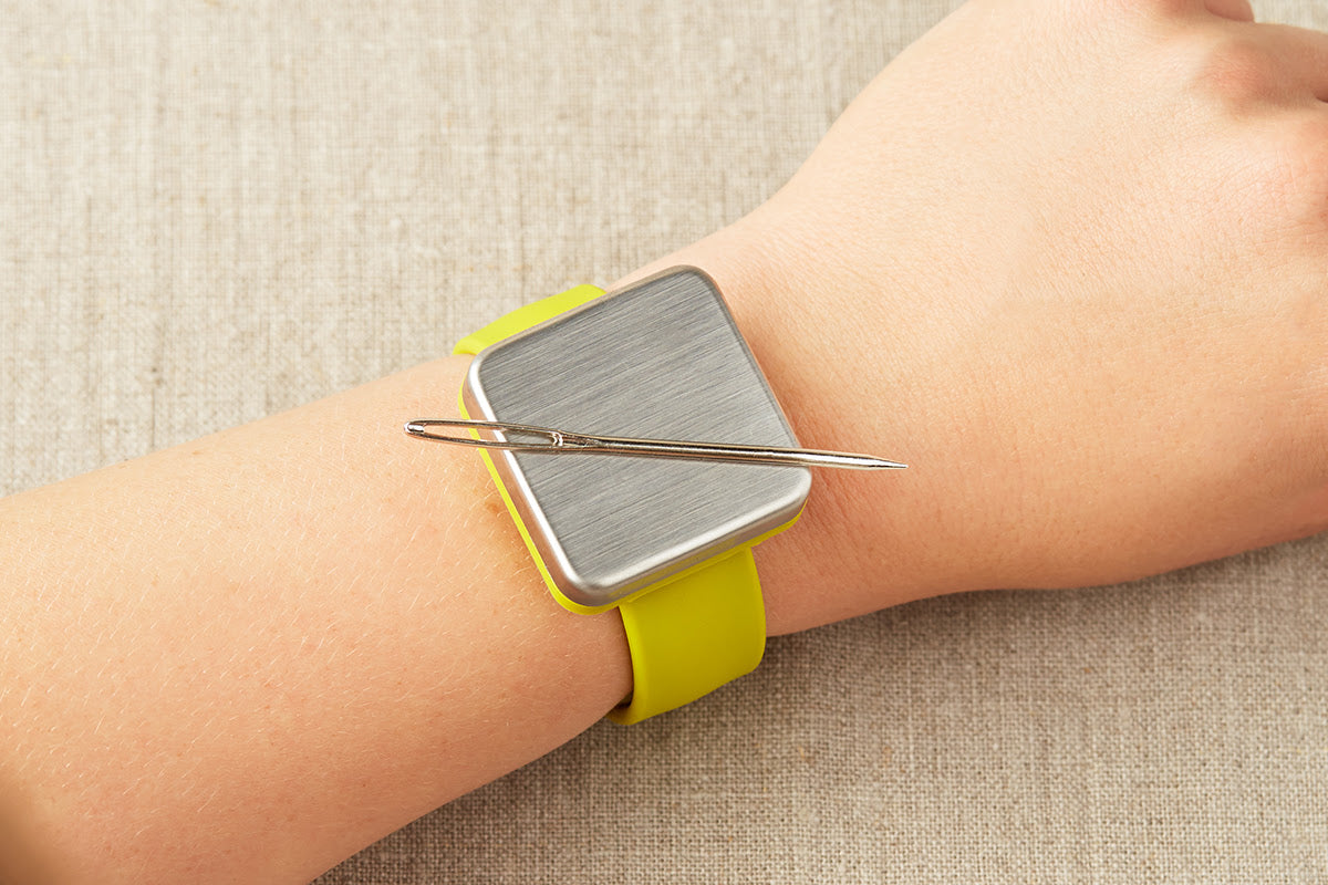 Yellow magnetic slap bracelet on a person's wrist with a darning needle attatched to the magnet.
