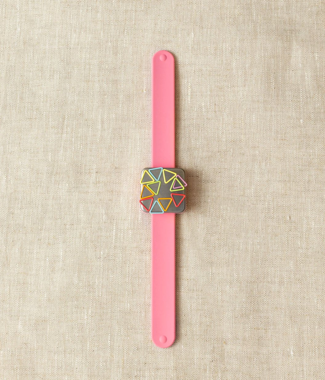 A pink silicone slap bracelet with a brushed steel-plated magnet in the center, holding geometric stitch markers.
