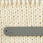 The back of a notions holder bracelet with imperial and metric system measurements, measuring a knitted swatch.
