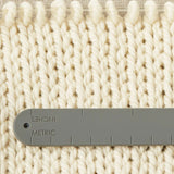 The back of a notions holder bracelet with imperial and metric system measurements, measuring a knitted swatch.